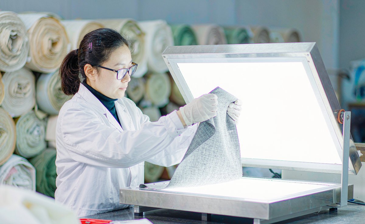 Technician checking fabric weave density against a light box - GorgeousBen fabric test report guide